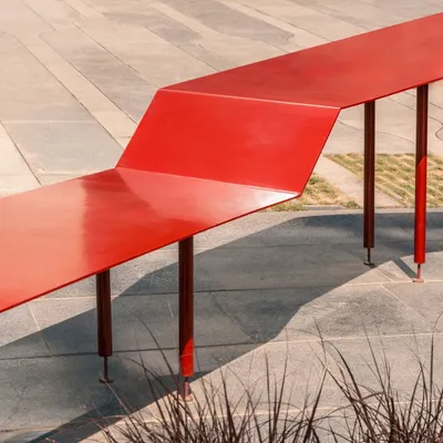 A detail of the Red Ribbon Plaza. The bright red, powder-coated steel is folded to create a continuous surface that functions as both a bench and a table, providing a playful and highly functional piece of urban furniture for a tech campus in Bangalore.