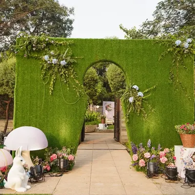 Welcome to Wonderland. The entrance to this themed baby shower features a grass wall with a keyhole arch, flanked by whimsical props like the White Rabbit and giant mushrooms.