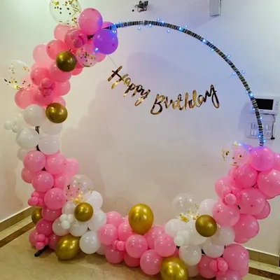 A simple yet elegant semi-arch balloon decoration for a birthday. This design uses a beautiful color palette of pink, white, and gold, with a 'Happy Birthday' banner and integrated fairy lights.