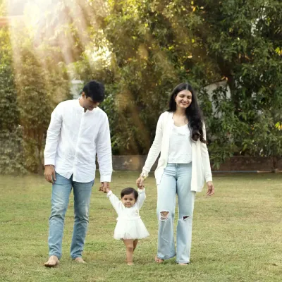 A heartwarming photo of parents holding their little girl's hands as she takes her first steps across a sunlit park lawn.
