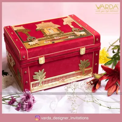 This opulent red velvet trunk is a statement piece for a grand wedding. Adorned with golden motifs inspired by traditional Indian architecture, it is designed to be a magnificent keepsake box long after the celebration.