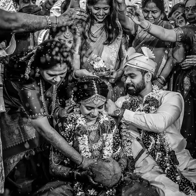 This black and white image captures the intensity and joy of a wedding ritual. The high contrast and surrounding family members create a powerful, timeless scene focused on the couple.