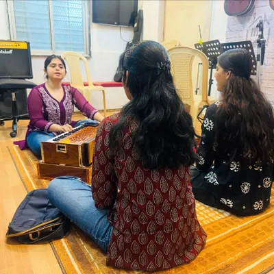 A Hindustani vocal class in session. Students sit with the instructor and a harmonium, learning the fundamentals of Indian classical singing in a traditional and focused setting.