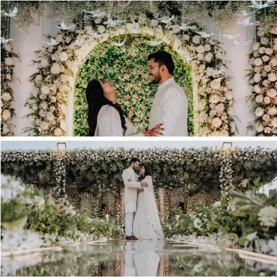 A beautiful couple portrait from an elegant green and white themed engagement. The backdrop is a stunning arch of white flowers and greenery, with whimsical glass birds hanging from above.