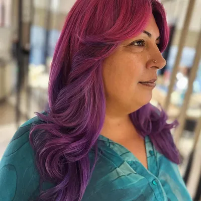 A fun and vibrant look with curtain bangs and face-framing layers. The pink and violet hair color makes a bold statement, and the cut adds beautiful shape.