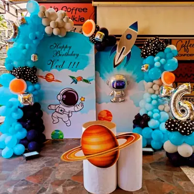 An out-of-this-world space-themed birthday party for Ved. This setup includes a large balloon arch in shades of blue, astronaut and rocket cutouts, planet props, and a personalized backdrop to create an exciting adventure for the birthday boy.