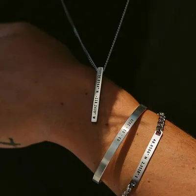 This image showcases a matching set for him, featuring a silver-toned bar necklace and two engraved bracelets. It's a perfect example of how to create a coordinated, personal look.