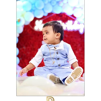 An adorable portrait of a one-year-old boy in a cute blue vest, sitting happily amidst balloons at his first birthday party.