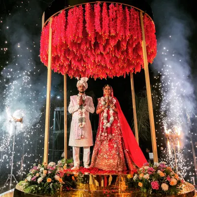 A Varmala that feels like it's floating in the heavens. We designed this elevated circular stage with a dense canopy of red florals, surrounded by cold pyros, to create a truly magical and unforgettable moment for the couple.