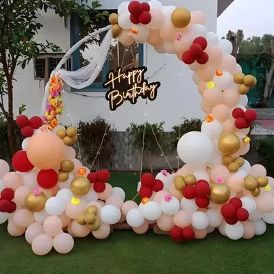 I also create decor for birthdays, like this beautiful outdoor balloon arch. The arrangement uses pastel, red, and gold balloons and features a 'Happy Birthday' neon sign, perfect for a garden party.