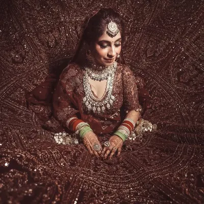A breathtaking top-down shot of the bride, seated within the magnificent spread of her heavily embroidered wedding lehenga. This artistic angle showcases the grandeur of the bridal attire.