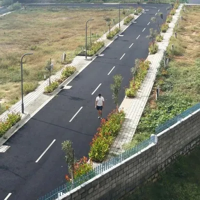 An aerial view of our completed BTM Meadows layout, showing the clean geometry of the asphalt road, paved sidewalks, and regularly spaced streetlights. The planted medians with young trees and shrubs are designed to mature into a green canopy over time.