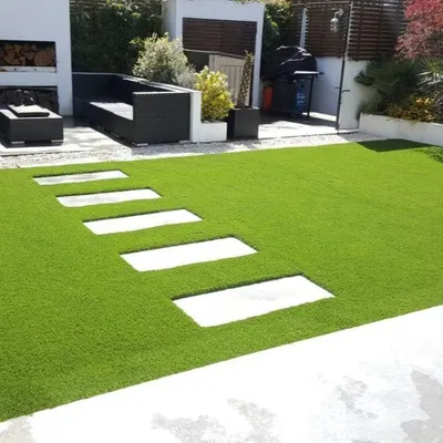 This modern patio design features clean lines with rectangular stone pavers set into a field of vibrant artificial grass. It creates a sophisticated and practical outdoor lounge area that is always ready for guests.