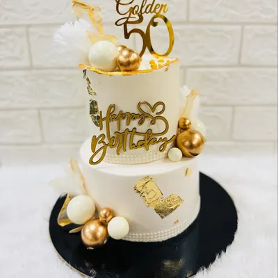 Celebrating a golden 50th birthday with this stunning two-tiered cake. It's decorated with white and gold spheres, gold leaf, and elegant toppers for a truly luxurious feel.