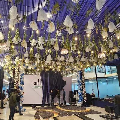 A full view of a massive birthday party decoration I executed. The ceiling is covered in blue fabric, with hanging greenery, lights, and disco balls to create a magical, starry night theme.