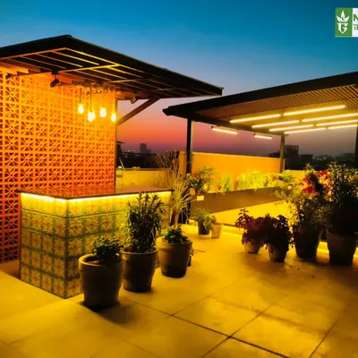 A stunning custom bar on a Gurgaon terrace, featuring a backlit patterned tile front and a terracotta jaali screen. The warm lighting creates an inviting atmosphere for evening drinks.