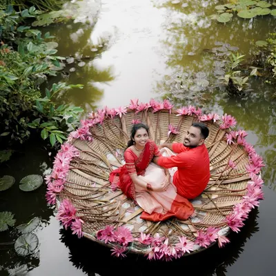 An aerial view of a couple floating on a traditional coracle decorated with water lilies. This unique perspective captures the tranquility and romance of the Kerala backwaters.