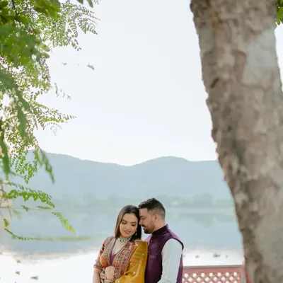 A tender moment captured by the lake, framed by the leaves of a tree. The soft light and natural setting create a peaceful and romantic atmosphere for this pre-wedding portrait.