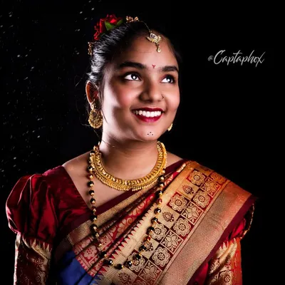 A joyful portrait of a model in a traditional Marathi-style saree. The studio lighting is set to highlight the rich colours of the fabric and the intricate gold jewellery, creating a warm and celebratory image.