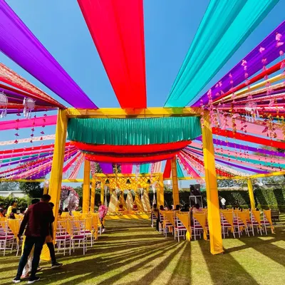 A wide view of a vibrant Haldi setup, with a canopy of multi-colored drapes creating a festive and energetic atmosphere for the celebration.