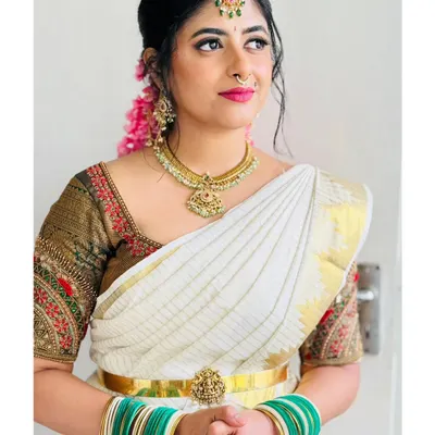 A classic South Indian bridal look with a white and gold saree, temple jewelry, and jasmine flowers. This is a perfect reference for a traditional wedding music performance.
