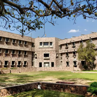The main academic block at IIHMR, built with a pinkish-grey quartzite sourced from a nearby village. The design uses traditional elements like precast *jaalis* and *chajjas* to create a building that is modern yet deeply connected to local craft.