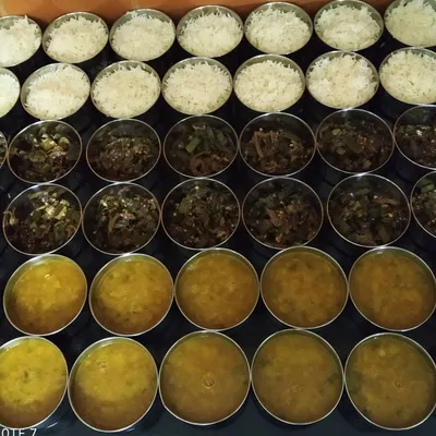 Preparing a bulk order of tiffins for an office in Greater Noida. Each component, from the bhindi sabzi to the dal and rice, is portioned carefully to ensure everyone gets a perfect meal.