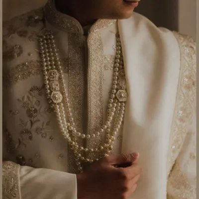 A close-up shot of the groom's royal attire, focusing on the intricate pearl necklaces and the fine embroidery of his sherwani. This detail shot speaks of elegance and tradition.