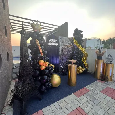 A complete view of the stylish black and gold rooftop party, featuring a miniature Eiffel Tower, balloon Christmas trees with gold chains, and a sequin backdrop.
