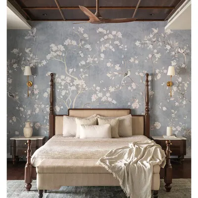 The master bedroom at Tinted Tapestries is a dreamy, tranquil sanctuary. The focal point is a custom four-poster bed in dark wood, set against an exquisite wallpaper adorned with delicate floral and avian motifs.