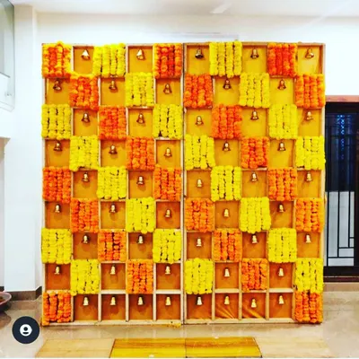 This unique backdrop is constructed from a wooden grid, with each section holding marigold flowers and a small brass bell. It's a visually stunning design that adds a beautiful sound element to the celebration.