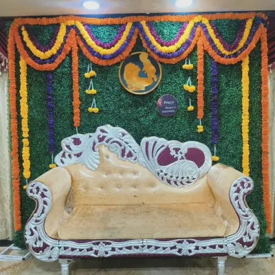 A classic stage setup for a traditional baby shower, featuring an ornate sofa against a green grass wall backdrop with marigold flower garlands.
