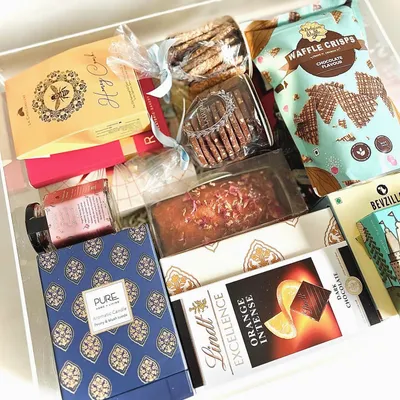 This is the epitome of luxury gifting. A custom acrylic trunk filled with an unparalleled selection of premium goods, including a Ladurée tea cake, Lindt Orange Intense chocolate, and a scented candle from Pure Home & Living.