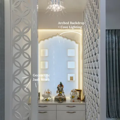 A serene white mandir featuring circular jaali panels, an arched backdrop with warm cove lighting, and luxurious marble flooring. This design transforms a prayer space into the heart of the home.
