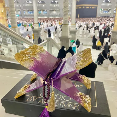 This custom Quran holder in a regal purple and gold design is shown at the holy site of Makkah. The piece is adorned with crystals and pearls and comes with a matching crystal tasbih.