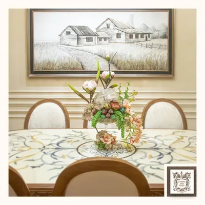 This dining setting showcases a classic marble inlay table, where each piece is carefully placed to create a harmonious design. The elegant floral centerpiece and rustic farmhouse wall art complete this picture of refined country living.