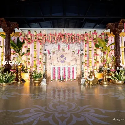 A wide view of the magnificent stage for Dhanvith's naming ceremony. The design incorporates carved wooden pillars, intricate floral arrangements, and a custom floor decal to create a complete, immersive, and traditional experience.