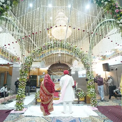 A wide-angle view of the Anand Karaj ceremony, showing the beautifully decorated Gurudwara and the couple taking their laavan. This shot captures the spiritual atmosphere of a Sikh wedding.