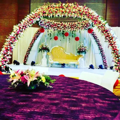 A full view of one of our grand stage designs, perfect for a wedding reception or anniversary. The combination of a dense floral arch, a classic chaise lounge, and strategic lighting creates a truly regal setting.