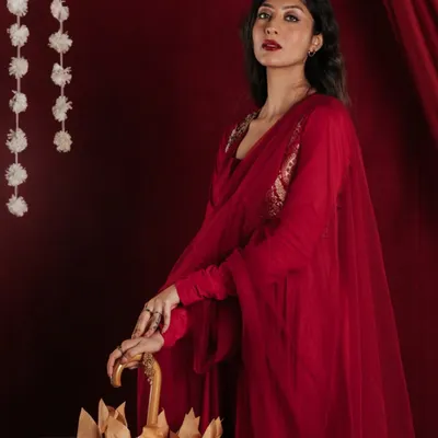 This studio shot focuses on the interaction between the model and the designer umbrella. The pose is directed to highlight the product's unique shape and handcrafted details, set against a rich, deep red that complements the model's attire.