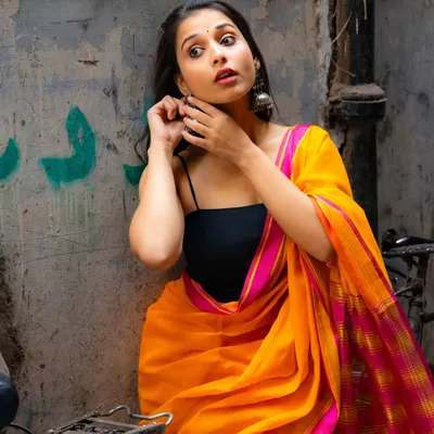 A candid moment in a quiet Delhi alley. The bright orange and pink saree pops against the weathered walls, creating a beautiful, spontaneous portrait.