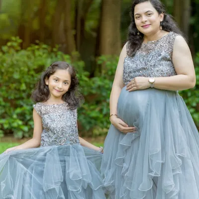 A perfect match. Our grey embellished gowns for mom and daughter feature sparkling bodices and layered tulle skirts, creating an elegant and cohesive look for a family maternity shoot.
