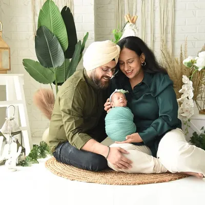 A happy family portrait with parents and their newborn, set against a bright and airy boho-themed backdrop. These full-family shots are perfect for celebrating your new arrival together.
