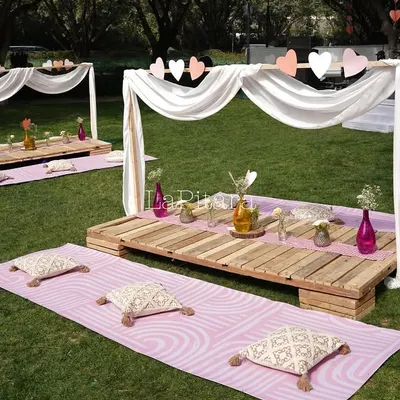 A charming low-seating picnic setup for a Valentine's brunch. We used wooden pallets as tables, surrounded by comfortable cushions on pink mats and framed by a simple white canopy draped with hearts.