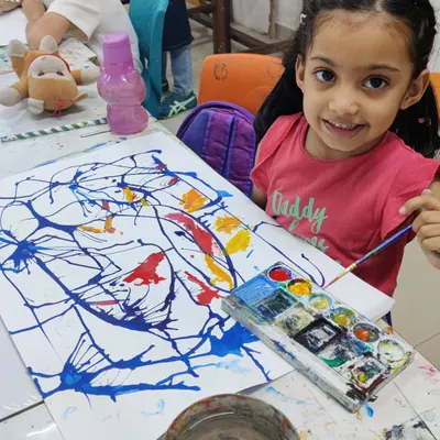 A very young artist smiles for the camera, delighted with her colorful abstract splatter painting. We believe in making art fun and accessible for all ages.