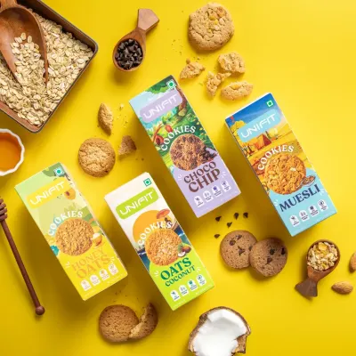 A flat lay of Unifit's cookie range, showcasing four different packaging designs along with their corresponding ingredients like oats, honey, and coconut.