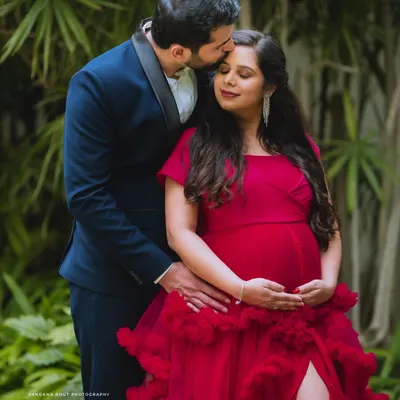 A tender moment captured during an outdoor maternity shoot. The vibrant red gown adds a touch of glamour, while the focus remains on the couple's loving connection.