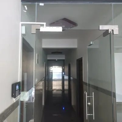 An installed biometric access control system in a typical office corridor. The setup seamlessly integrates with the frameless glass doors, ensuring security without compromising the office aesthetic.