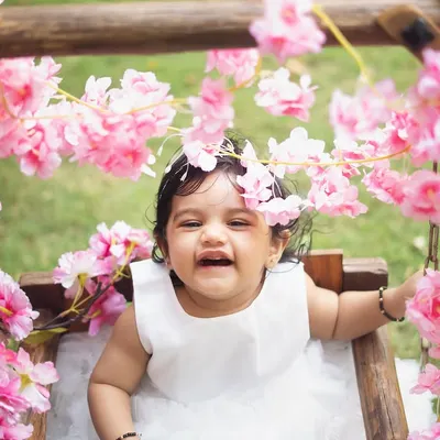 Pure, uninhibited laughter. This little girl is having the best time on a floral swing during her outdoor first birthday shoot. The natural light and greenery create a beautiful, vibrant setting.