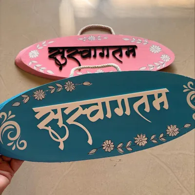 A pair of 'Suswagatam' welcome boards in pink and teal. These oval hangings are perfect for adding a warm, traditional welcome to your entrance.